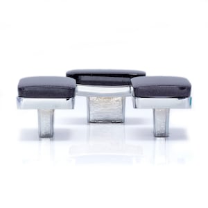 Könnte beinhalten: Drei Schrankknöpfe mit quadratischen, dunkelgrauen Oberteilen und polierten Chrombasen. Die Knöpfe sind in einer Reihe angeordnet, wobei der mittlere Knopf etwas größer ist. Die Hardware ist vor einem weißen Hintergrund platziert.