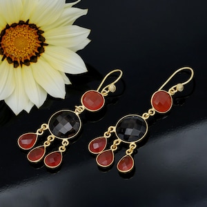 May include: Gold-toned dangle earrings with red and black gemstones. Each earring features a red circular stone at the top, a faceted black circular stone in the middle, and three red teardrop-shaped stones hanging below.