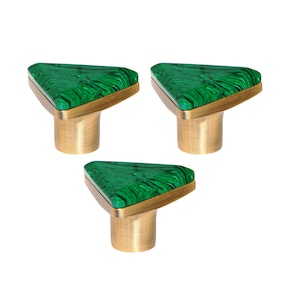 May include: Three cabinet knobs. Each has a triangular, malachite-style green top with a brass base and gold-coloured trim. These knobs are designed for furniture and home decor. The knobs are suitable for use in the home.