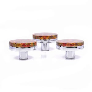 Op de afbeelding: Drie decoratieve kastknoppen met een kleurrijk, gespikkeld ontwerp in tinten rood, oranje, geel en groen. De knoppen hebben een ronde bovenkant en een gepolijste chromen basis. Deze hardware-accenten zijn ideaal om een unieke touch aan meubels toe te voegen.