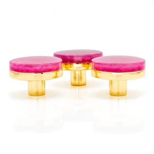 Könnte beinhalten: Drei dekorative Schrankknöpfe mit goldfarbenem Sockel und einem rosa, kreisförmigen Oberteil. Die Knöpfe haben ein modernes Design und sind vor einem weißen Hintergrund platziert. Die Knöpfe sind wahrscheinlich aus Metall und Harz.