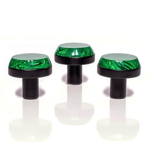 May include: Three cabinet knobs with a green, marbled glass top and a black base and stem. The knobs are displayed against a white background. The knobs are likely for furniture.