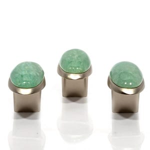 May include: Three cabinet knobs featuring a light green, rounded stone top and a brushed metal base. The knobs are displayed in a row against a white backdrop, highlighting their design and texture.