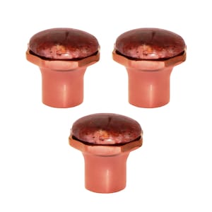 Pode incluir: Três puxadores de armário cor de cobre com um tampo de pedra manchada castanho-avermelhada. Os puxadores têm uma base cilíndrica e um detalhe hexagonal em torno do tampo de pedra. Os puxadores são exibidos sobre um fundo branco.