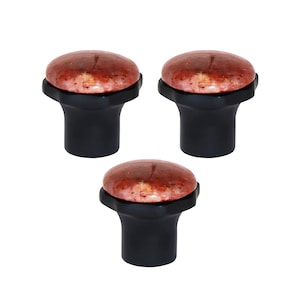 Może przedstawiać: Trzy dekoracyjne gałki do szafek. Każda gałka ma zaokrąglony, nakrapiany, czerwonobrązowy wierzch i czarną, cylindryczną podstawę. Gałki ułożone są w trójkąt na białym tle.