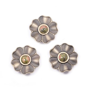 Könnte beinhalten: Drei blütenförmige Schrankknöpfe mit Bronze-Finish. Jeder Knopf hat einen zentralen Stein mit grünen und rosa Farbtönen. Die Knöpfe sind auf weißem Hintergrund angeordnet und zeigen ihr dekoratives Design.