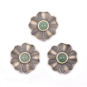 May include: Three flower-shaped decorative knobs. Each knob has a bronze-colored metal finish with a green gemstone center. The knobs are arranged on a white background. These knobs are suitable for furniture or craft projects.