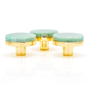 Può includere: Tre pomelli decorativi per mobili con una parte superiore rotonda in pietra verde chiaro e una base dorata. I pomelli hanno un design moderno e sono su uno sfondo bianco. I pomelli sono probabilmente utilizzati per mobili o armadi.