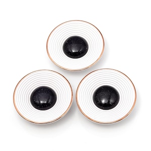 Puede incluir: Tres objetos redondos decorativos con un anillo exterior blanco estriado, un centro oscuro y un borde cobrizo. Los objetos están dispuestos en un patrón triangular sobre un fondo blanco.