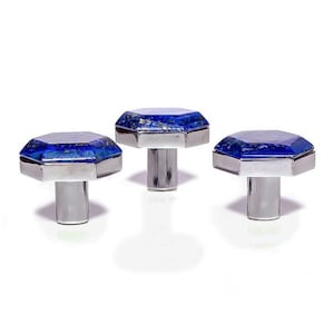 Puede incluir: Tres gemelos plateados con caras octogonales de piedras preciosas azul oscuro. Las piedras preciosas tienen un aspecto moteado y están engastadas en un bisel plateado. Los gemelos tienen un poste cilíndrico.