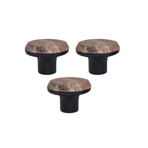 May include: Three cabinet knobs. Each has a round top with a pattern in brown, pink, and beige, and a black cylindrical base. The knobs are arranged in a triangular pattern against a white background.