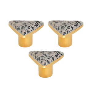 May include: Three cabinet knobs with a triangular top featuring a speckled pattern in black and grey. The knobs have a gold-coloured, V-shaped frame and a cylindrical base. These decorative knobs are ideal for furniture upgrades.