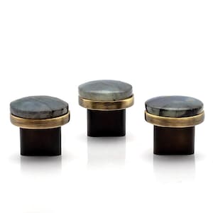 May include: Three cabinet knobs with a grey, oval stone set in a gold-coloured metal band. Each knob sits on a dark brown, rectangular base. The knobs are displayed against a white background.