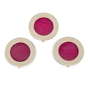 May include: Three circular cufflinks with a gold-tone border and a magenta centre. These accessories are designed for formal attire. The image is set against a white backdrop, emphasizing the details of the cufflinks.