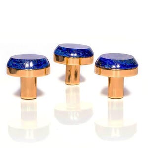 Könnte beinhalten: Drei goldfarbene Schrankknöpfe mit pilzförmigem Design. Jeder Knopf hat eine kreisförmige Oberseite mit einem blau-weißen Marmormuster, das von einem goldenen Band umrahmt wird. Die Knöpfe sind vor einem weißen Hintergrund platziert und erzeugen eine saubere, moderne Ästhetik.