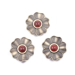 May include: Three decorative flower-shaped cabinet knobs. Each knob features a bronze-colored metal flower with a red center. The knobs are arranged on a white background, showcasing their design and color.