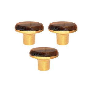 May include: Three cabinet knobs with a brown, oval top and a gold-coloured base. The knobs are arranged in a triangular pattern. The knobs are suitable for furniture. The background is white.