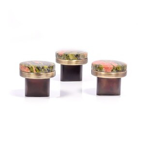 May include: Three cabinet knobs with a speckled stone top in green, red, and brown, set within a gold-coloured metal band. The knobs are mounted on dark brown, square bases. Each knob is a decorative item.