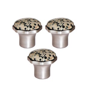 Op de afbeelding: Drie kastknoppen met een gespikkelde, beige en zwarte stenen bovenkant en een geborstelde zilveren basis. De knoppen hebben een afgeronde bovenkant en een facetrand waar de steen de basis raakt. De basis is cilindrisch met een uitlopende, achthoekige bovenkant.