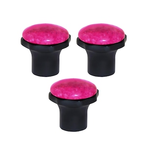 May include: Three cabinet knobs with a decorative design. Each knob has a bright pink, oval top with a speckled texture, mounted on a black, cylindrical base. The knobs are evenly spaced against a white background.