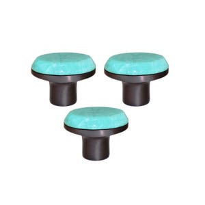 May include: Three cabinet knobs with a light turquoise top and a dark brown base. The knobs are arranged in a triangular pattern. The knobs are suitable for drawers or cabinets.