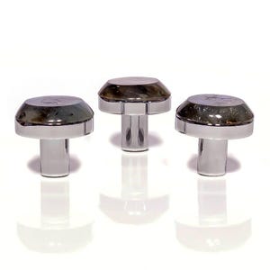 May include: Three cabinet knobs with a mushroom design. Each has a polished silver base and a domed, translucent top with a smoky, marbled look. The knobs are arranged on a white surface, reflecting light. The knobs are suitable for cabinets.