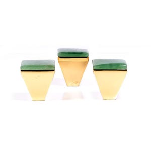 Könnte beinhalten: Drei goldfarbene, geometrische Boxen mit grünen Deckeln. Die Boxen haben eine trapezförmige Form mit flacher Oberseite und einem grünen, quadratischen Deckel. Die Boxen sind auf weißem Hintergrund angeordnet.