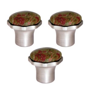May include: Three cabinet knobs with a natural stone appearance. Each knob has a rounded, oval top with a mottled pattern of green and red hues, set on a brushed silver-toned metal base. The knobs are designed for furniture or cabinetry.