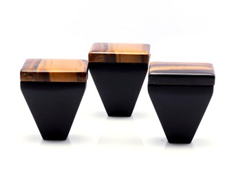 Könnte beinhalten: Drei schwarze, geometrisch geformte Boxen mit quadratischen Deckeln aus Tigeraugenstein. Die Boxen sind vor einem weißen Hintergrund angeordnet. Die Deckel haben braune und goldene Farbtöne.