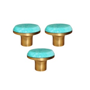 Può includere: Tre pomelli decorativi per mobili con una parte superiore turchese sfaccettata e una base color oro. I pomelli hanno una forma rotonda e sono su sfondo bianco. Questi pomelli sono ideali per aggiungere un tocco di eleganza ai mobili.