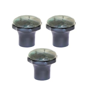 May include: Three cabinet knobs with a dark grey base and a rounded, oval-shaped top. The top has a marbled appearance with shades of green, grey, and white. The knobs are set against a white background.