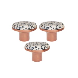 Op de afbeelding: Drie decoratieve kastknoppen. Elke knop heeft een gespikkelde, gebroken witte en zwarte bovenkant, met een koperkleurige basis. De knoppen zijn paddenstoelvormig en staan tegen een witte achtergrond.