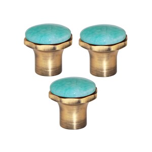 May include: Three cabinet knobs with a teal, rounded stone top and a brass-coloured base. The knobs have a decorative, vintage-inspired design, suitable for furniture or home decor projects.