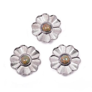 Könnte beinhalten: Drei silberfarbene, blütenförmige Zierknöpfe mit strukturierter Oberfläche. Jeder Knopf hat einen zentralen, runden, gesprenkelten, olivgrünen und braunen Stein. Die Knöpfe sind auf weißem Hintergrund angeordnet.