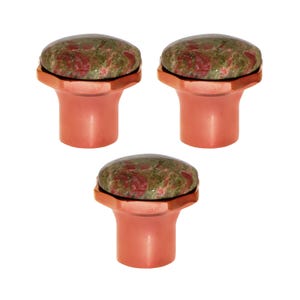 May include: Three cabinet knobs with a copper finish. Each knob has a round, polished stone top with a mottled pattern of green and red hues. The knobs are designed for furniture or decorative use.