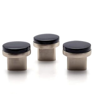 Può includere: Tre pomelli per mobili dal design moderno. Ogni pomello presenta una parte superiore circolare in pietra nera, una fascia in metallo color argento e una base rettangolare. I pomelli sono esposti su sfondo bianco.