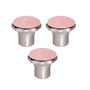 Pode incluir: Três puxadores de armário com um topo arredondado rosa claro e uma base prateada escovada. Os puxadores têm um design moderno e estão sobre um fundo branco. Estes puxadores são adequados para móveis ou armários.