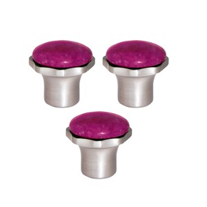 May include: Three cabinet knobs with a brushed silver base and a round, magenta-coloured stone top. The knobs have a modern design and are set against a white background. Suitable for drawers and cabinets.