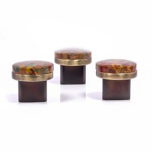 May include: Three decorative cabinet knobs. Each knob has a dark brown square base, a brass-coloured band, and a colourful, speckled top with shades of red, yellow, and green. The knobs are set against a white background.