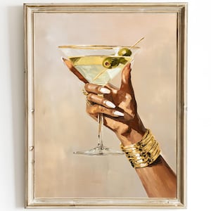 May include: A framed painting depicts a hand holding a martini glass with olives. The glass has a gold rim and is filled with a light green liquid. The hand is adorned with gold jewelry and a gold bracelet. The background is a soft beige.