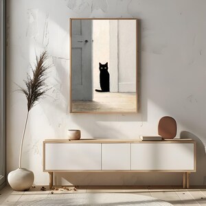 Peut inclure: Une impression d'art encadr&eacute;e repr&eacute;sentant un chat noir assis dans une porte. L'&oelig;uvre d'art a un style minimaliste avec une palette de couleurs neutres. Le cadre est de couleur bois clair, et le chat est le point central.