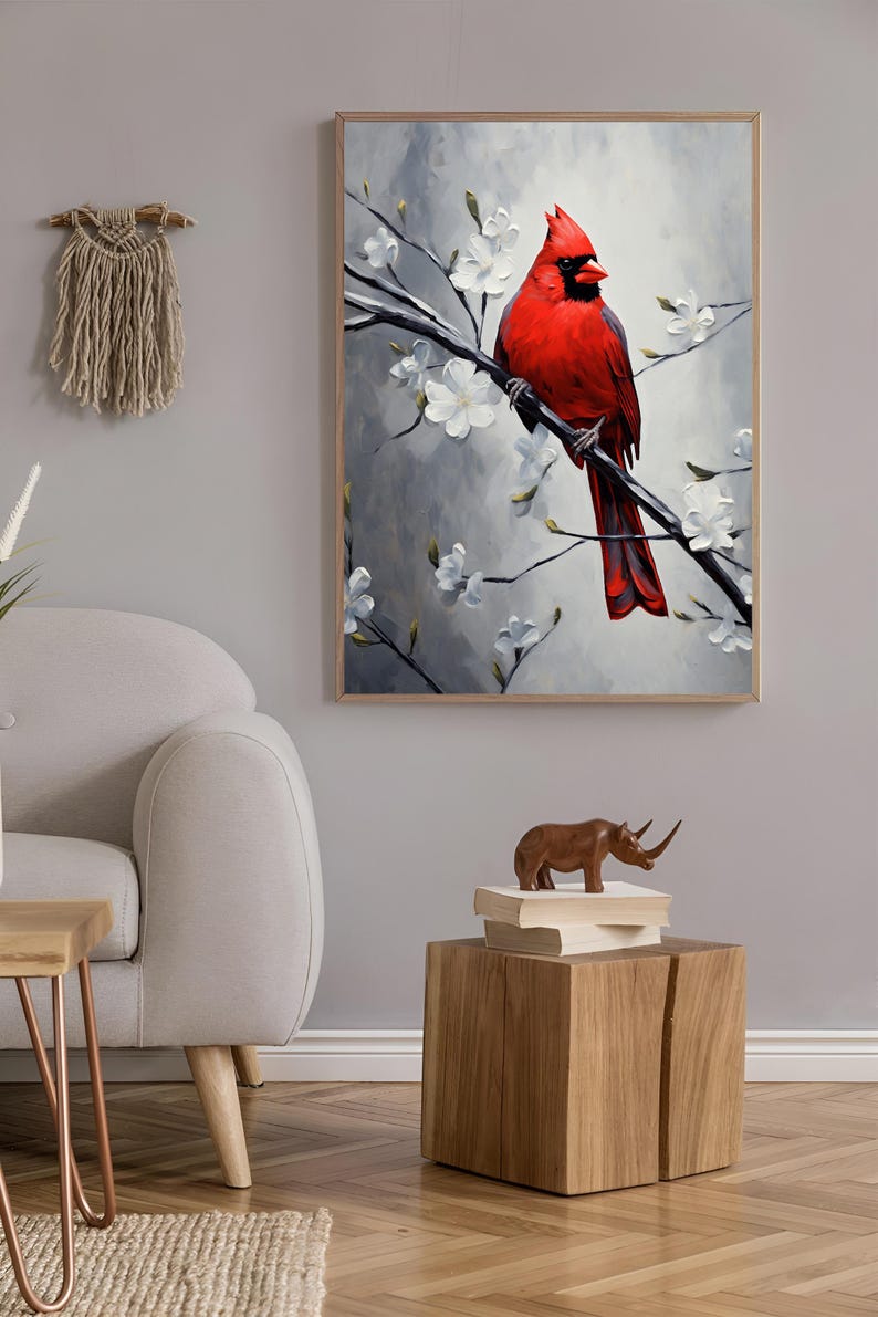May include: A framed painting of a vibrant red cardinal perched on a branch with white blossoms. The artwork is set against a soft gray background, creating a serene and natural aesthetic. The painting is displayed in a living room setting.