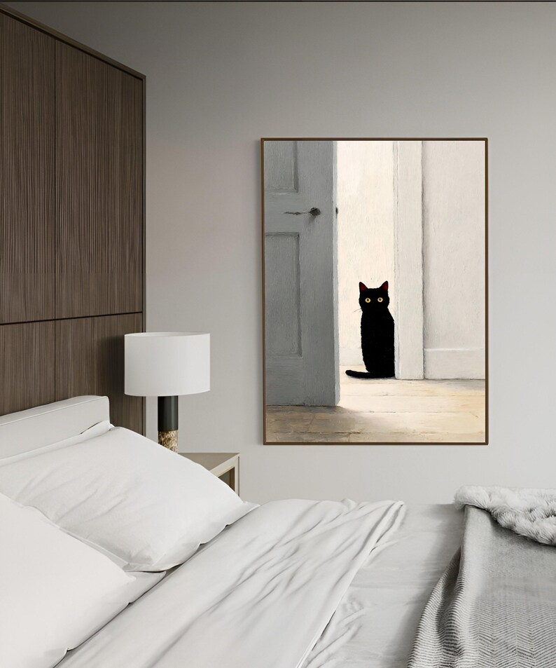Peut inclure: Une impression d'art encadr&eacute;e repr&eacute;sentant un chat noir aux yeux jaunes dans une embrasure de porte. Le chat est au centre, devant une porte gris clair et des murs blancs. L'&oelig;uvre a un style minimaliste.