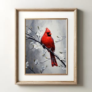 May include: A framed art print featuring a vibrant red cardinal perched on a branch with white blossoms. The bird is set against a soft gray and white background. The frame is a light gold color.