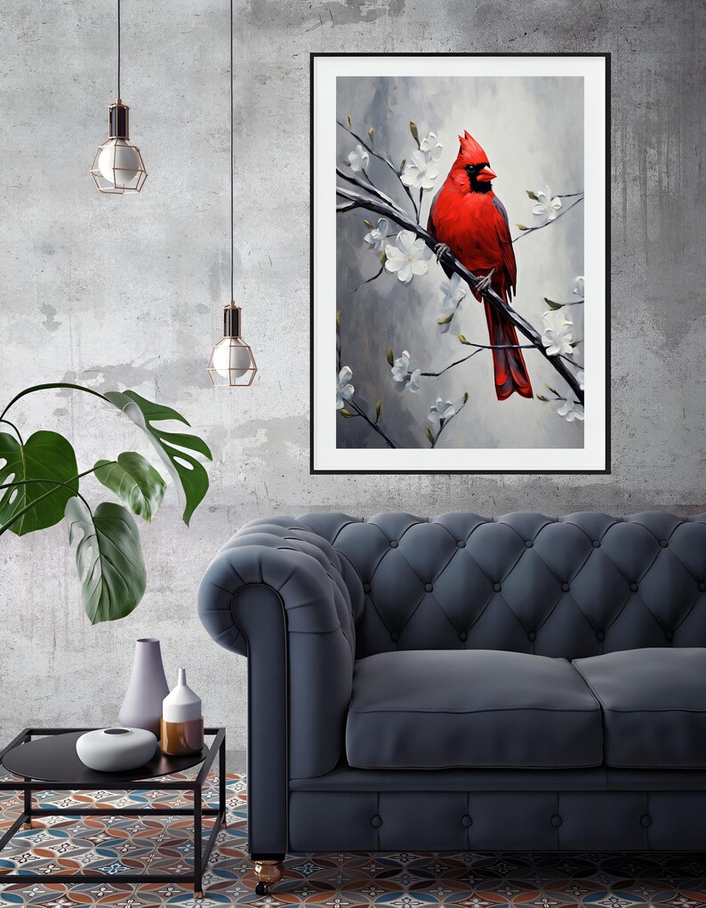 May include: A framed art print featuring a vibrant red cardinal perched on a branch with white blossoms. The artwork is set against a soft gray background, creating a striking contrast. The print is displayed in a living room setting with a blue sofa and decorative elements.