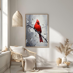 May include: A framed art print featuring a vibrant red cardinal perched on a branch with white blossoms. The bird is set against a soft gray and white background, creating a serene and natural scene. The artwork is displayed in a light-colored wooden frame.