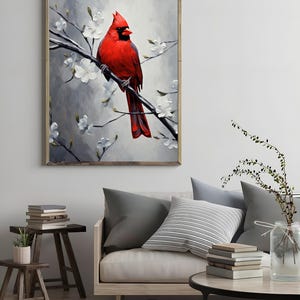May include: A framed artwork featuring a vibrant red cardinal perched on a branch with white blossoms. The bird's feathers are detailed against a soft, gray background. The artwork is displayed in a living room setting.