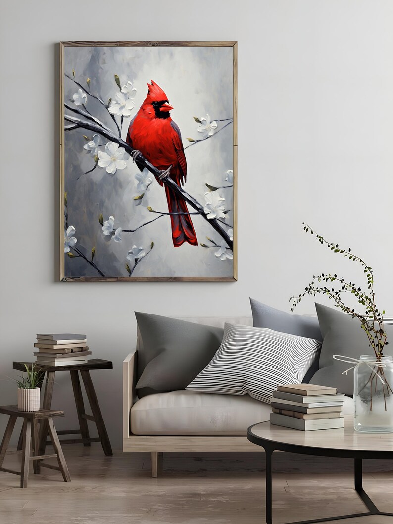 May include: A framed artwork featuring a vibrant red cardinal perched on a branch with white blossoms. The bird's feathers are detailed against a soft, gray background. The artwork is displayed in a living room setting.
