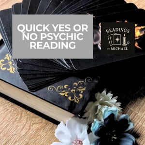 May include: A stack of black tarot cards with gold accents, resting on a decorative book. The image includes text that reads "Quick Yes or No Psychic Reading" and a logo that says "Readings by Michael". White and blue flowers are in the foreground.