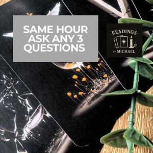 May include: A close-up of tarot cards with a black background. The cards have a white dove and yellow flower design. Text on the cards reads "SAME HOUR ASK ANY 3 QUESTIONS" and "READINGS by MICHAEL". Green plant in the background.